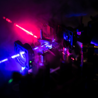 Photo of a dark lab with optical elements and laser beams of different wavelengths