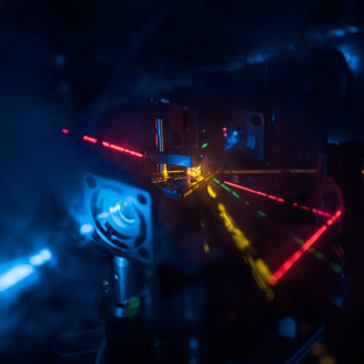 Photo of a dark lab with optical elements and laser beams of different wavelengths