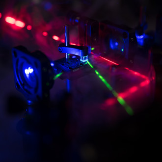 Photo of a dark lab with optical elements and laser beams of different wavelengths