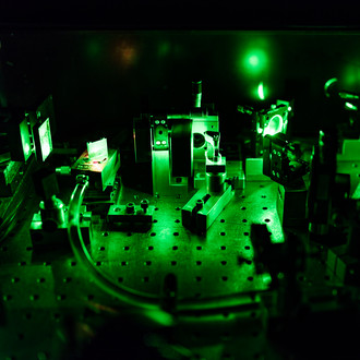 Photo of a dark lab with optical elements and a green laser beam