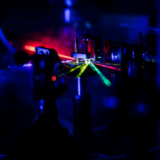 Photo of a dark lab with optical elements and laser beams of different wavelengths